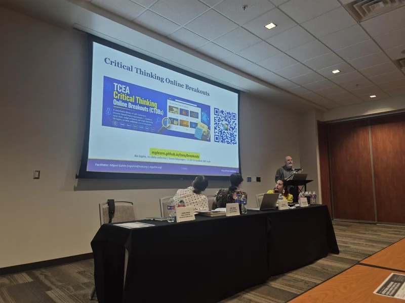 Presenter beside a projected Critical Thinking Online Breakouts slide and a seated panel.