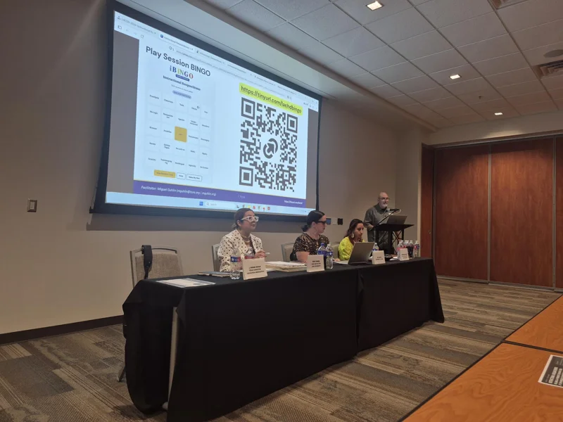 Panelists and presenter beneath a projected presentation resources slide with a QR code.